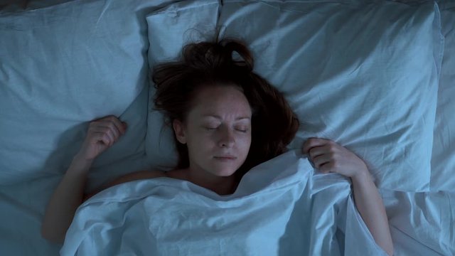 Someone pulls  duvet blanket  with sleeping woman at night. She covers her face with horror hands.
