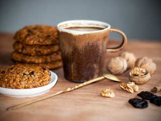 oatmeal cookies, brown mug with cocoa, walnuts, cinnamon, prunes, vintage spoon on the wooden table