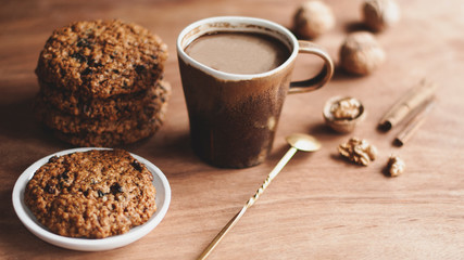 oatmeal cookies, brown mug with cocoa, walnuts, cinnamon, prunes, vintage spoon on the wooden table