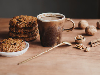 oatmeal cookies, brown mug with cocoa, walnuts, cinnamon, prunes, vintage spoon on the wooden table