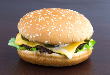Burger on a table made of wood. Beef patty burger, cheddar cheese, lettuce, bacon, pickled cucumber, tomato and balsamic sauce.