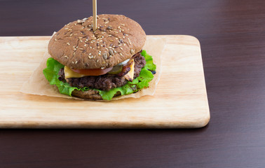 Big Burger on a table made of wood. Beef patty burger, cheddar cheese, lettuce, bacon, pickled cucumber, tomato and balsamic sauce.