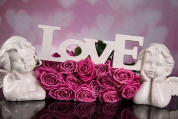 A bouquet of pink roses against a black background with love angels