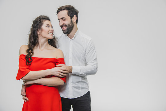 A Man And A Woman With Long Hair, Supporting Each Other With Love. Valentine's Day. A Woman Dressed In A Red Dress Of A Man In A White Shirt.