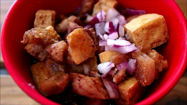 Handheld close up video shot of a bowl of chopped fried pork and tofu with soy sauce