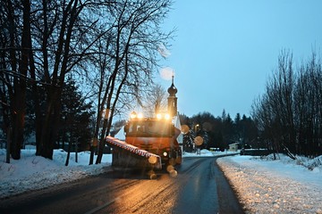 Front view of snowplow service truck - gritter car spreading salt on the road. Maintenance of roads in winter in the mountains.