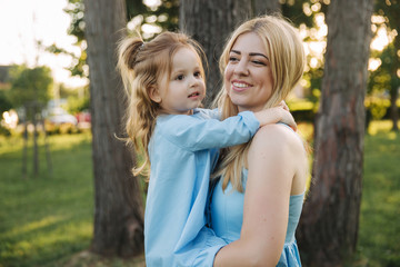 Fototapeta premium Young beautiful woman with her little cute daughter. Young daughter hugs mother in summer park