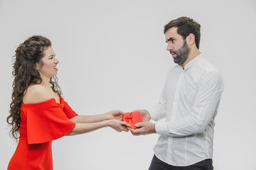 Young couple loving. A man made a present for his wife. During this time, the red field is presented in the form of a heart. Wife is pleasantly surprised. Dressed in a red dress and a white shirt.