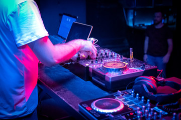 DJ music console and laptops in bright colors of light in night club bright blue background