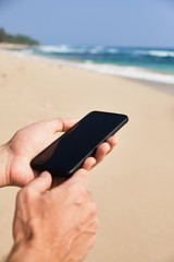 Mobile phone in male hand on the background of the beach and ocean.
