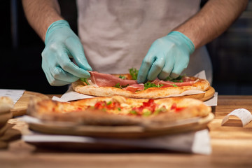 Obraz na płótnie Canvas Chef making a parma or prosciutto ham Italian pizza in a close up view of his hands placing the meat