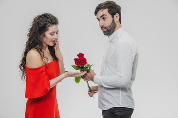 A young man hiding a bunch of roses behind his surprise to astonish his girlfriend for Valentine's Day. Dressed in red dress and white shirt.