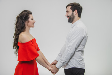 Young tender and in love couple. Hold hands with each other looking straight into your eyes. Dressed in red dress and white shirt.