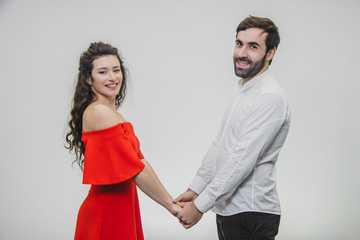 Young tender and in love couple. Hold hands at each other looking straight at the smile. Dressed in red dress and white shirt.