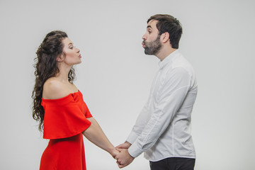 Young tender and in love couple. Keep hands on each other looking straight at wanting to kiss. Dressed in red dress and white shirt.