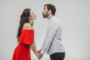 Young tender and in love couple. Keep hands on each other looking straight at wanting to kiss. Dressed in red dress and white shirt.