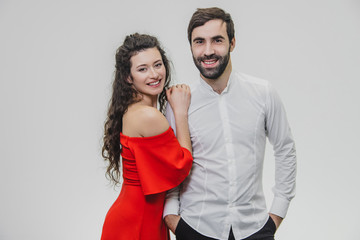 Man and woman with long hair. The wife put her hands on the shoulder of her husband with love. Valentine's Day. A woman dressed in a red dress, a man in a white shirt.