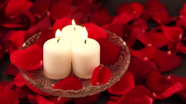three burning candles stand in red rose petals