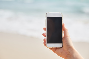 Mobile phone in female hand on the background of the beach and ocean