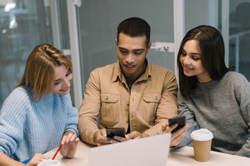 Group of multiracial hipster friends with emotional smiling faces using smartphone and  mobile app for mobile banking, shopping online, booking tickets. University students learning language together.