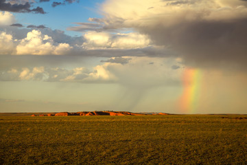 Fototapeta premium Rainbow and rain clouds at Bajandsag (Flaming Cliffs) in Gobi Desert during sunset with magical clouds and dramatic sky (Gobi Desert, Mongolia, Asia)