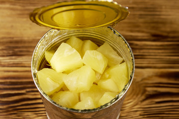 Opened tin can of pineapple pieces on wooden table