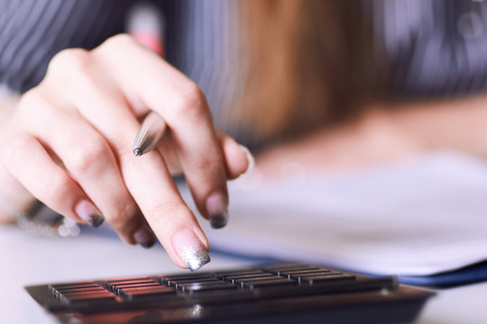 Business woman hand using a calculator with silver pen in office closeup.