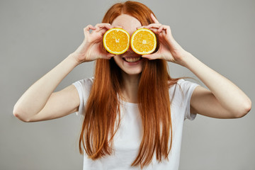 healthy lifestyle, pleasant girl with long red hair holding oranges near the face and posing to the camera