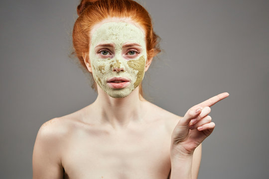 pleasant girl with green clay mask pointing at somewhere. girl showing direction, way.