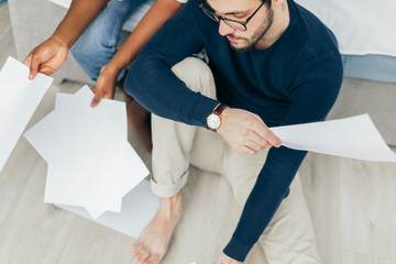 Obraz premium African and Caucasian mixed race married couple sitting on the floor at home checking unpaid bills, taxes, due debt, bank account balance. There is a time to gather the stones and a time to sum up.