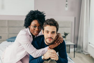 Portrait of young mixed race loving couple having romantic times in bedroom. African woman embracing affectionately her european american friend.