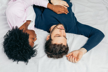 Positive delighted multiethnic couple sleeping together in bed on white sheets, happy traditional family concept.