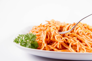 Spaghetti with pesto rosso decorated with parsley eaten with a fork on a white background