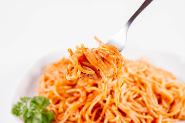 Spaghetti with pesto rosso decorated with parsley eaten with a fork on a white background