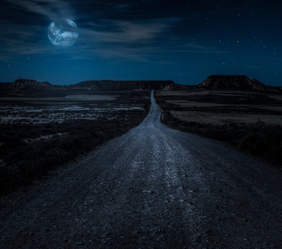 Moon, stars and clouds in the night. Wild west road illuminated from the moon. Moonlight and road background.