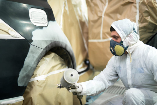 Man with protective clothes and mask painting automobile car bumper in repair shop.