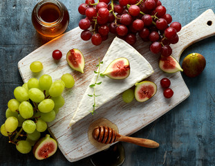 Cheese brie with figs, green and red grape and honey on white wooden board