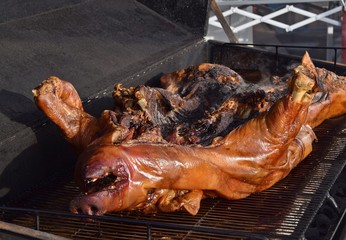 Ganzes, gegrilltes Schwein auf einem Grill im Rauch mit Salat und Orangen