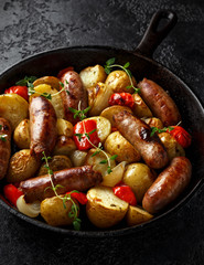 Homemade Pork sausages with potato, red pepper and onion in cast iron vintage pan.