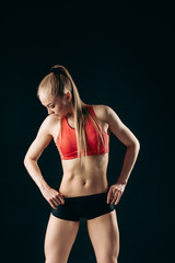 Fototapeta premium Muscular slender stylish girl standing looking down with her hands on hips on black background.close up shot.