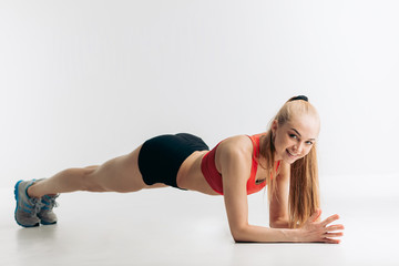 Fototapeta na wymiar cheerful blonde athlete showing plank exercises for tight, flat abs, full length side view shot