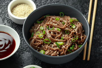 Soba noodles, buckwheat on a black bowl, with spring onion and sesame seeds. Traditional Japanese food.