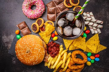 Fotobehang Junk food concept. Unhealthy food background. Fast food and sugar. Burger, sweets, chips, chocolate, donuts, soda, top view. © vaaseenaa