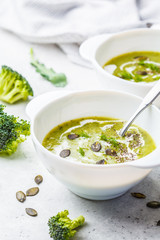 Vegan detox broccoli cream soup with coconut cream and pumpkin seeds in white bowl, copy space.