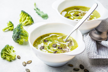 Vegan detox broccoli cream soup with coconut cream and pumpkin seeds in white bowl, copy space.