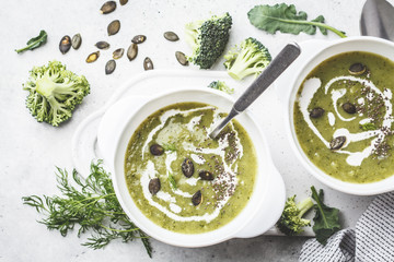 Vegan detox broccoli cream soup with coconut cream and pumpkin seeds in white bowl, top view.