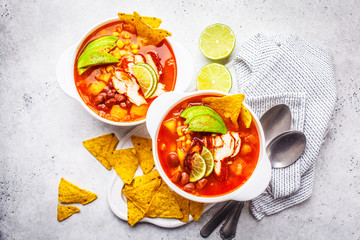 Mexican soup (Chili con carne) with beans, chicken, corn and nachos in white bowls - traditional mexican food.