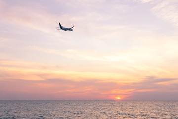 Obraz na płótnie Canvas Airplane flying above tropical sea at sunset