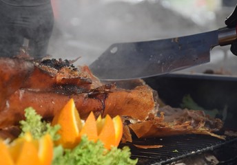 Ganzes, gegrilltes Schwein auf einem Grill im Rauch mit Salat und Orangen wird mit einem scharfen...