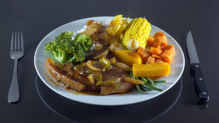 plate of pork chops and steamed vegetables on black background  
